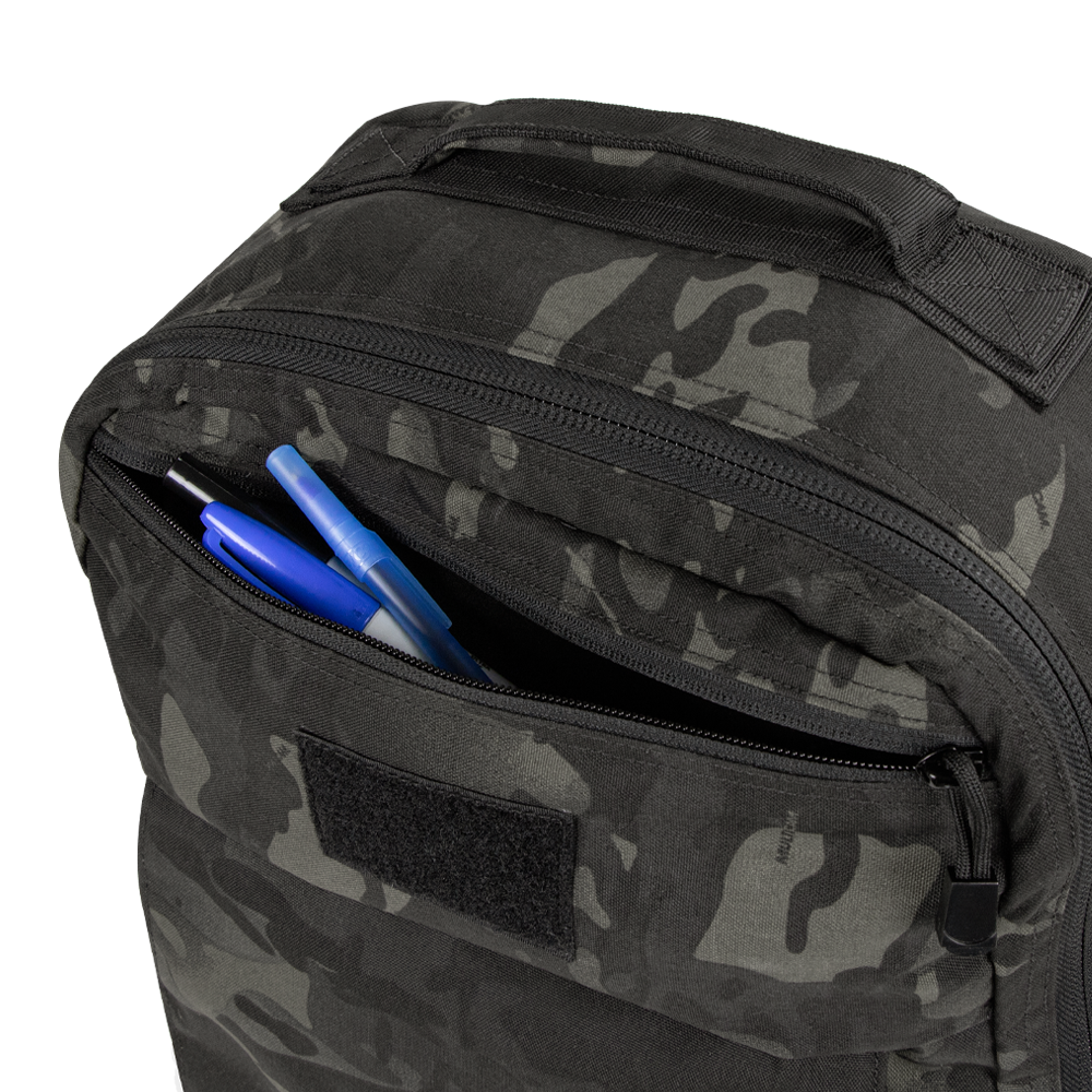 A close-up of the Condor Prime Pack 21L in MultiCam Black with its front zipper pocket open, revealing two blue pens and one black pen inside.